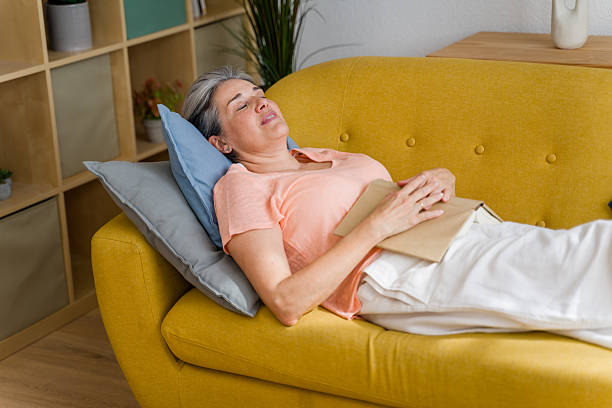 istock Senior woman sleeping on sofa with book on her belly 2224432804