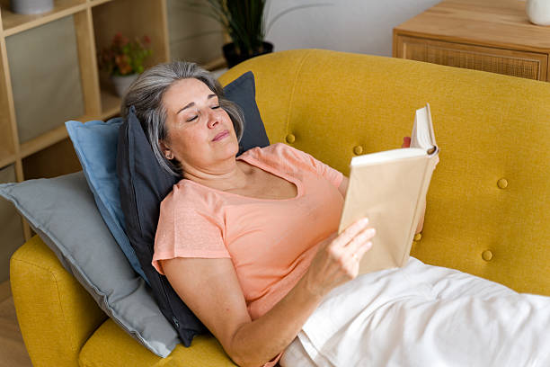 istock Senior woman relaxing on sofa reading a book at home 2224432816