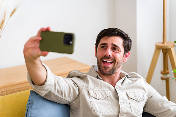 istock Young man taking a selfie with his smartphone while sitting on a couch 2224434569