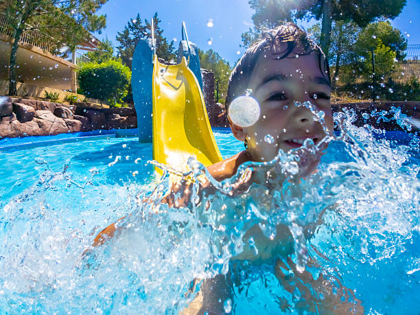 Happy child splashing joyfully in the pool while zooming down a water slide at a vibrant resort during a sunny summer vacation