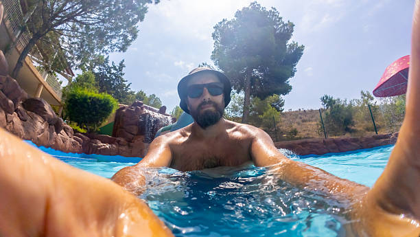 Mid adult man swimming in a tranquil pool surrounded by nature, capturing a moment of leisure and relaxation under the sun with clear blue water