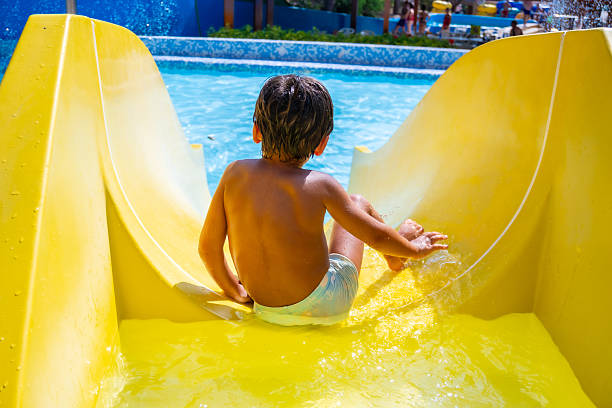 istock Child having fun sliding down a yellow waterslide in a water park 2224435517
