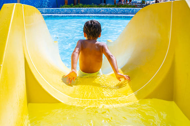Child joyfully sliding down a bright yellow waterslide into a sparkling swimming pool, enjoying a fun-filled summer day in the sun