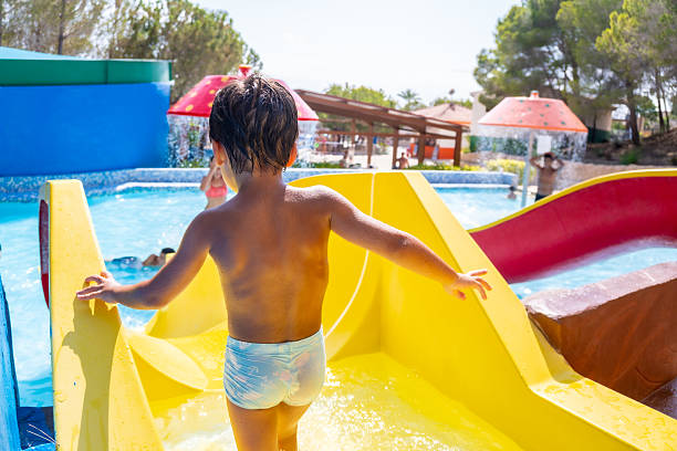 Child walking down a bright yellow waterslide at a vibrant water park, splashing joyfully in the refreshing summer sunshine