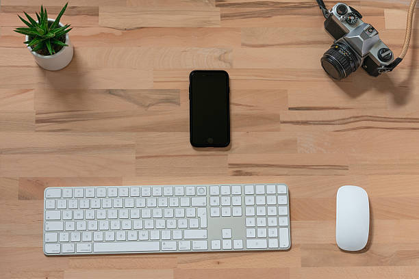 workspace of modern wireless mouse, white keyboard, smartphone and an analog film camera on wooden table with green plant. top view with copy space. flat lay as a background with copy space
