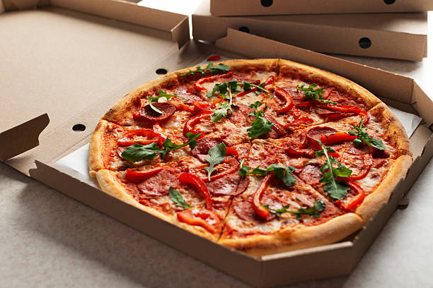 istock Large Pizza in open carton box on kitchen table closeup view 2224436091