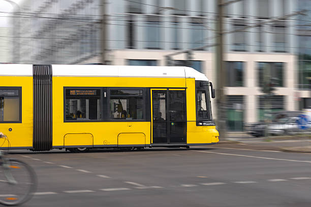 A yellow tram rushes through a city intersection with motion blur, capturing the pace and energy of modern urban life.