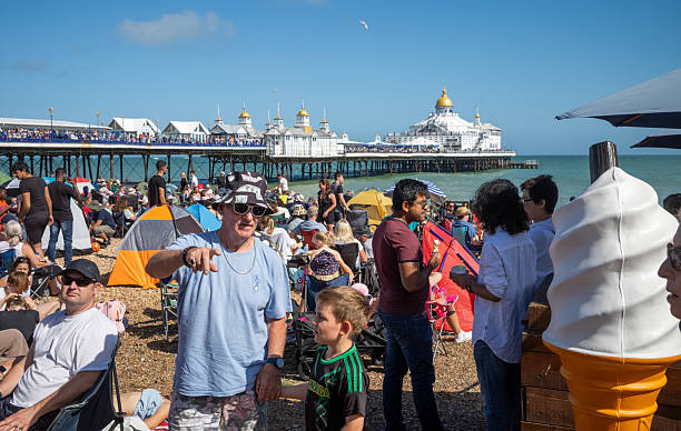 People crowd the beach next to Eastbourne Pier as they attend the annual Eastbourne Airbourne, an international airshow.\nThe show runs for four days each summer flying displays along the seafront.