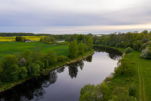 istock Scenic view of a calm river surrounded by lush greenery and fields at sunset 2224451755
