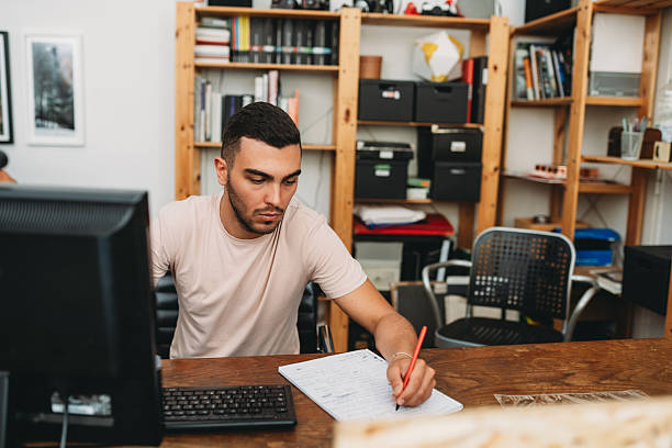istock Focused young man working at desk in home office writing notes 2224453164