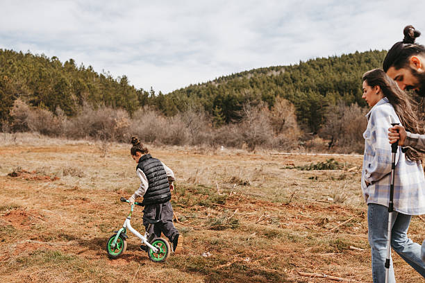Beautiful boy pushing his little bicycle while walking with parents along dirt road in nature
