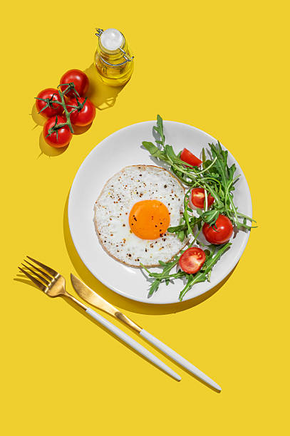 istock Fried eggs with arugula and cherry tomatoes on a white plate on a bright yellow background 2224463135
