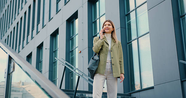 istock Pretty young smiling woman looking on watch while talking on smartphone during walking in urban city outdoors 2224470898