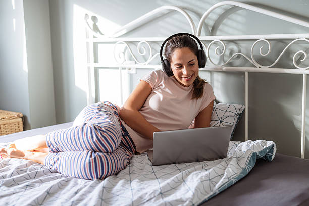 Woman relaxing on bed with headphones while using a laptop