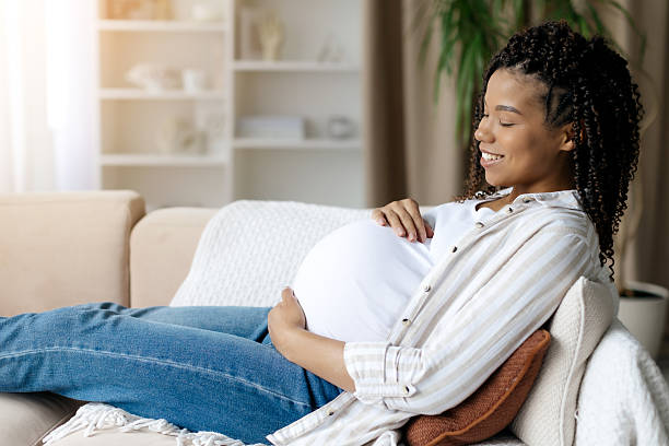istock Black pregnant woman resting on couch, smiling gently while holding belly 2224482272