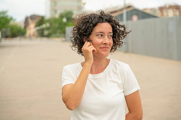 Mid adult woman adjusting her wireless earpiece while working outdoors in an urban environment