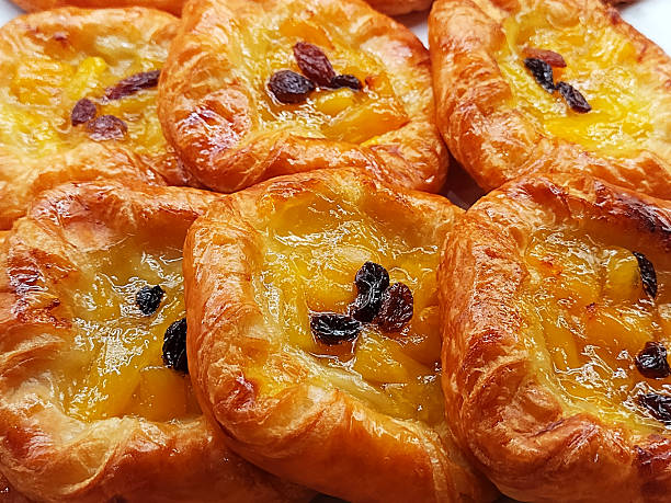Golden, flaky Danish pastries filled with sweet pineapple chunks and generously adorned with plump, dark raisins, a delightful tropical treat.