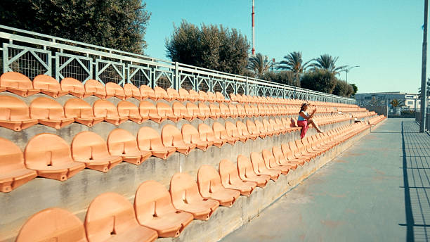 Woman sitting on the bleachers of an empty stadium, enjoying the sun and the peace