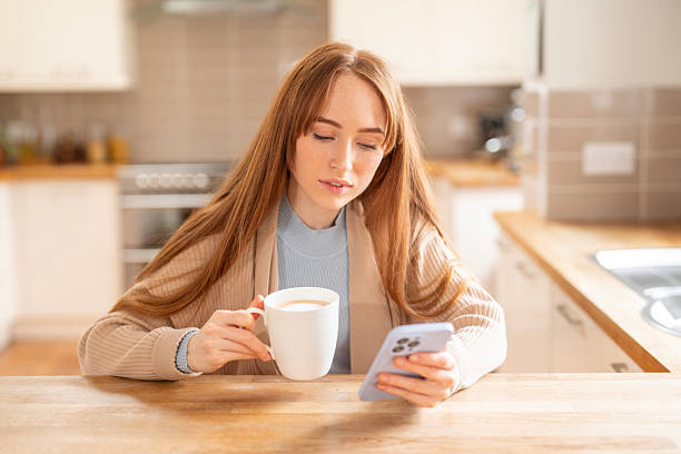 istock Woman enjoys a warm drink while browsing on her smartphone in a cozy kitchen during a relaxing morning at home 2224490952