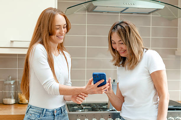istock Two women sharing a joyful moment while looking at a smartphone in a modern kitchen during the day 2224492783