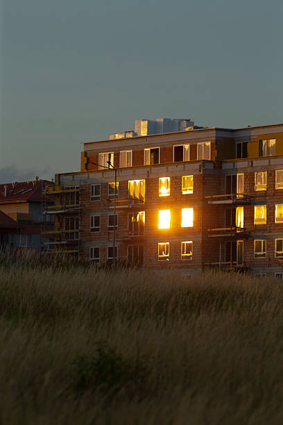 As twilight falls over the city, a charming apartment building glows warmly, its illuminated windows reflecting the serene essence of urban evenings and thoughtful architecture