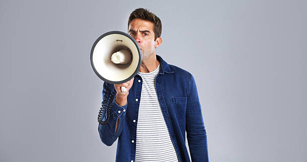 istock Portrait, megaphone and man in studio, screaming or justice with protest on white background. Facial expression, person or model with bullhorn, frustrated or activism for human rights, noise or angry 2224496540