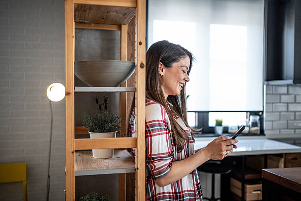 istock Young woman using smartphone and smiling in modern kitchen 2224497139