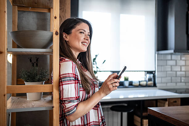 istock Young woman using smartphone and smiling in modern kitchen 2224497179