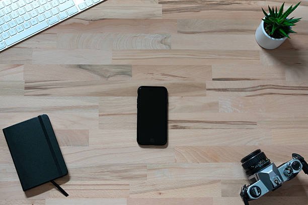 workspace of modern white wireless keyboard, smartphone, notebook and an analog film camera on wooden table with green plant. top view with copy space. flat lay as a background with copy space