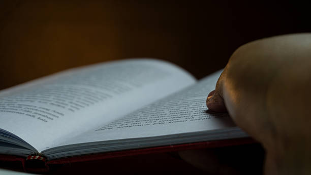 istock Hand holding open book with blurred text, warm spotlight on pages against dark background, intimate reading moment with soft focus and storytelling tone 2224500080