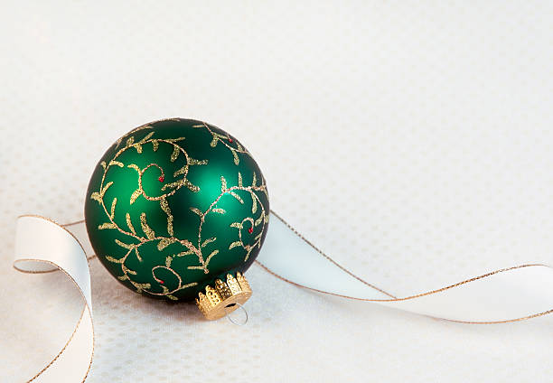 One ornate green Christmas ornament with white ribbon on white background with subtle pattern.
