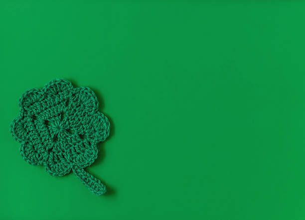 Green crochet shamrock or clover leaf cup coaster on a green background. Cop yspace. Top view. St. Patrick day concept.