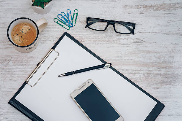 Office workplace table with blank paper page smartphone coffee cup and eyeglasses