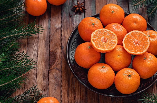 istock Christmas composition with fresh tangerines on a brown plate and fir tree branches on a dark wooden board. 2224508778