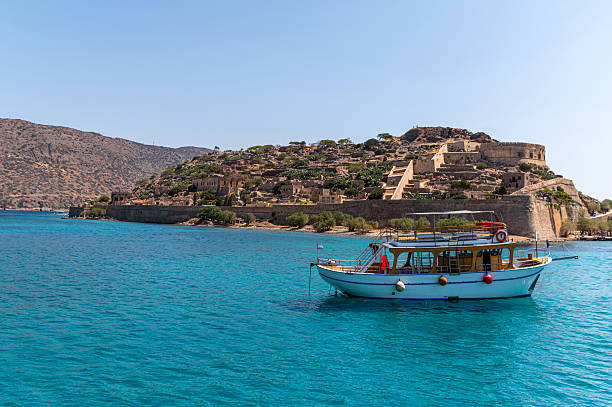A traditional boat sails near Spinalonga Island, showcasing ancient ruins and turquoise waters.