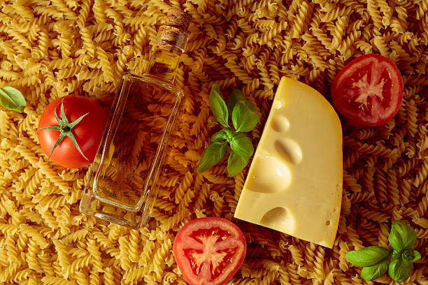Uncooked fusilli pasta with tomatoes, olive oil, basil and cheese. Italian cuisine. Top view.