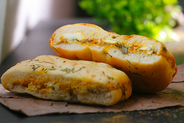 Delicious Indian stuffed paneer kulcha, sliced open to reveal spicy cottage cheese filling, placed on brown paper with scattered herbs.