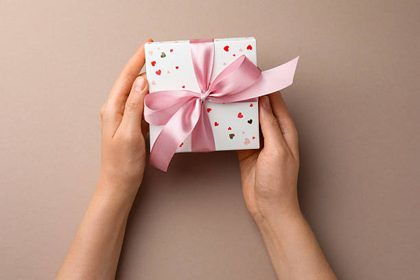 istock Woman holding gift box with pink bow on beige background, top view 2224512701