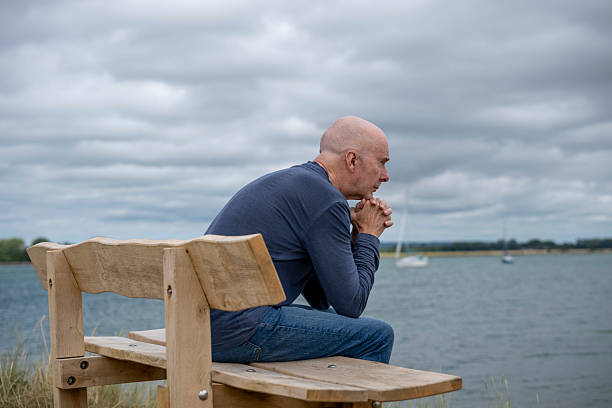 istock man sitting on a bench looking out to sea 2224516656