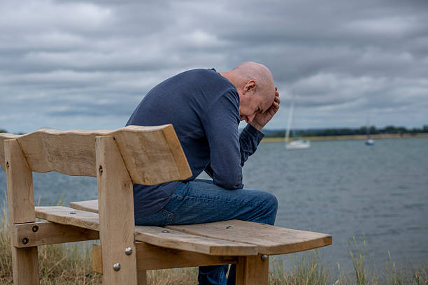 man sitting on a bench by the sea with head in hands