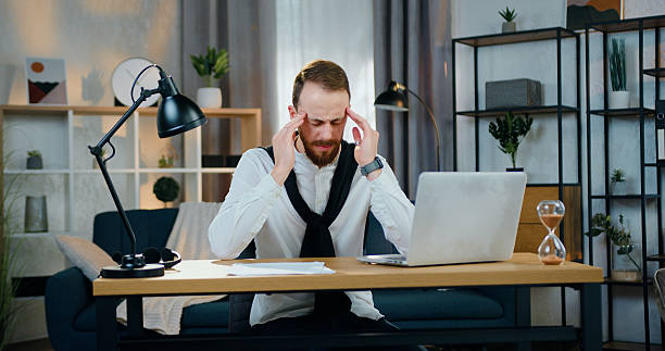 istock Tired attractive concentrated on work bearded office maanger sitting in home office working on laptop and with papers and then massaging temples because feelling headache 2224516881