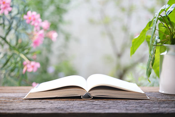 Opened old book on wooden table with romantic pink flowers background