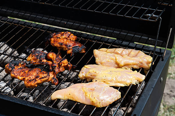 Marinated chicken thighs and breasts are cooking over a charcoal grill, with some pieces already beautifully charred and others still raw. The mix of textures and colors captures the dynamic process of outdoor barbecue preparation.