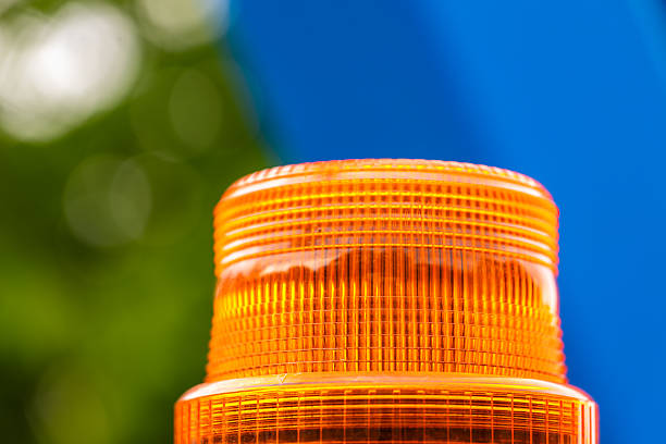 Close-up of an orange warning light against a blurred blue and green background, emphasizing the texture and color of the light.