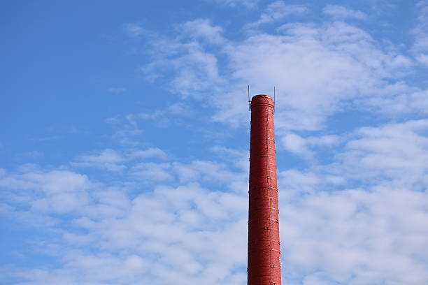A single red brick chimney stands alone in an open field, surrounded by green grass and possibly some trees.