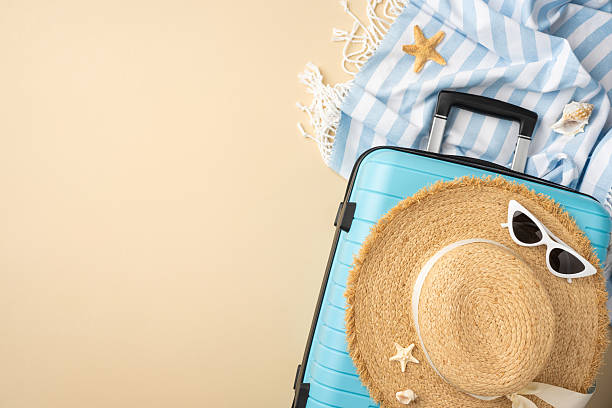 istock Top view of a vacation setup featuring blue suitcase, straw hat, and holiday items 2224532021