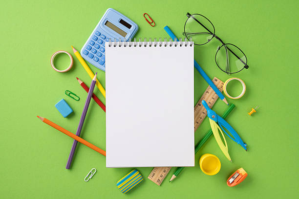 istock Artistic vertical arrangement of stationery objects including a notebook, calculator, and pencils surrounded by vibrant green 2224532025
