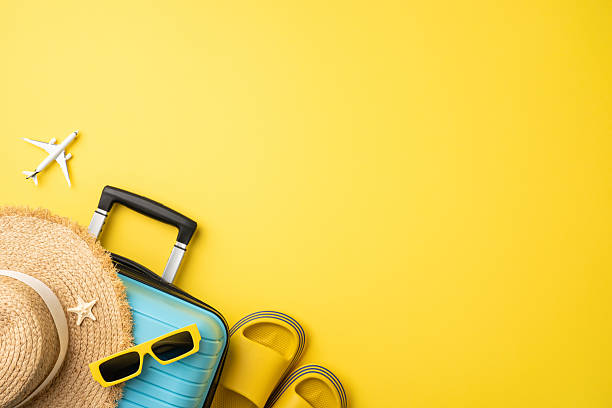 istock Travel essentials including a suitcase, straw hat, sunglasses, and sandals on a yellow backdrop, embodying vacation vibes. Plane and starfish add elements of summer travel and tropical destinations 2224532043