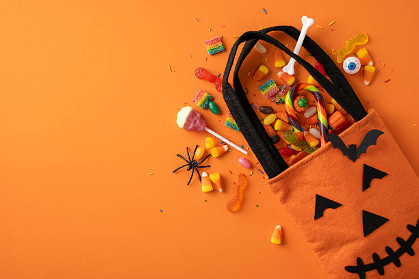 istock An orange Halloween bag with a pumpkin face spills candy and sweets on a solid orange background, evoking a festive Halloween atmosphere with vibrant colors and sugary treats 2224532048