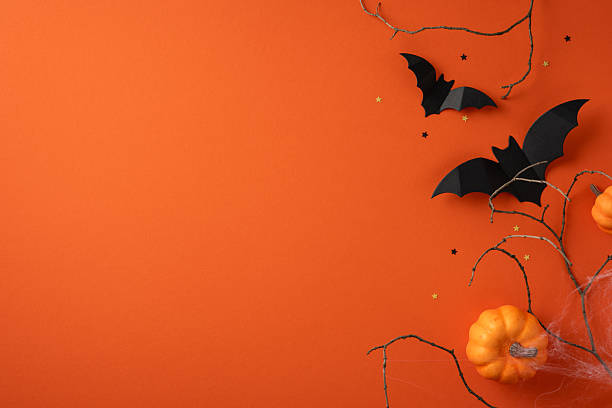 Halloween-themed image featuring black paper bats, orange pumpkins, and branches against an orange background